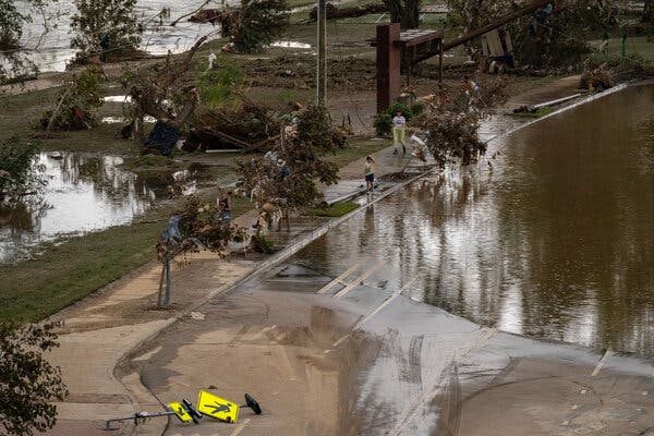 People examine damage from a storm, including a flooded street, downed trees and a toppled street sign.