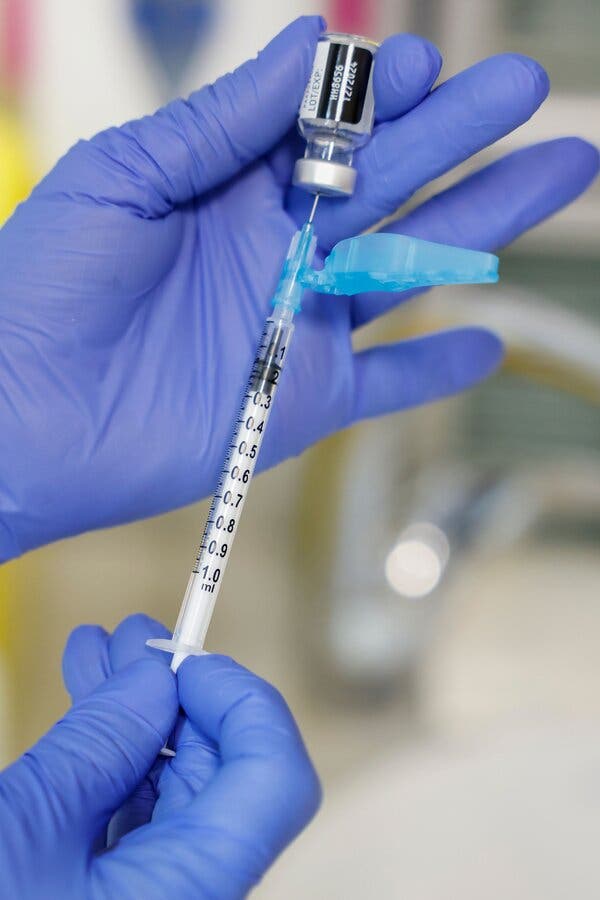 Two hands, each in a blue glove, fill a syringe from a vial.   