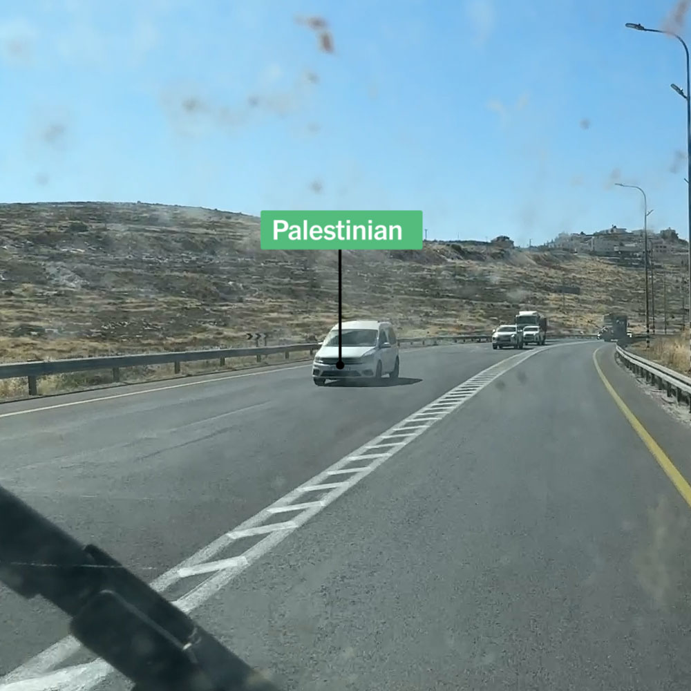 A two line road showing vehicles with Israeli and Palestinian license plates sharing the road.